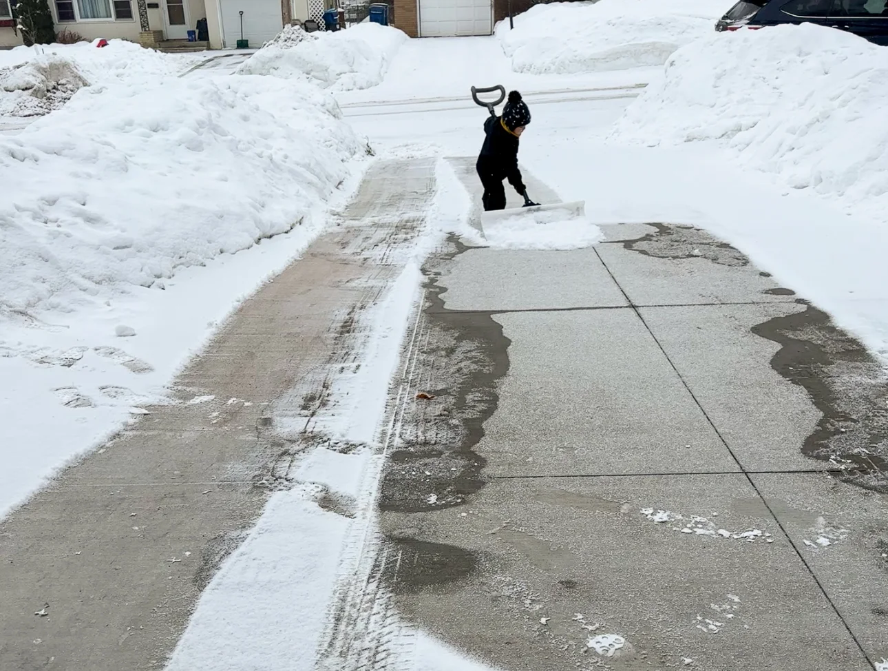 Montessori toddler plays in the outdoors during winter by shoveling a driveway.