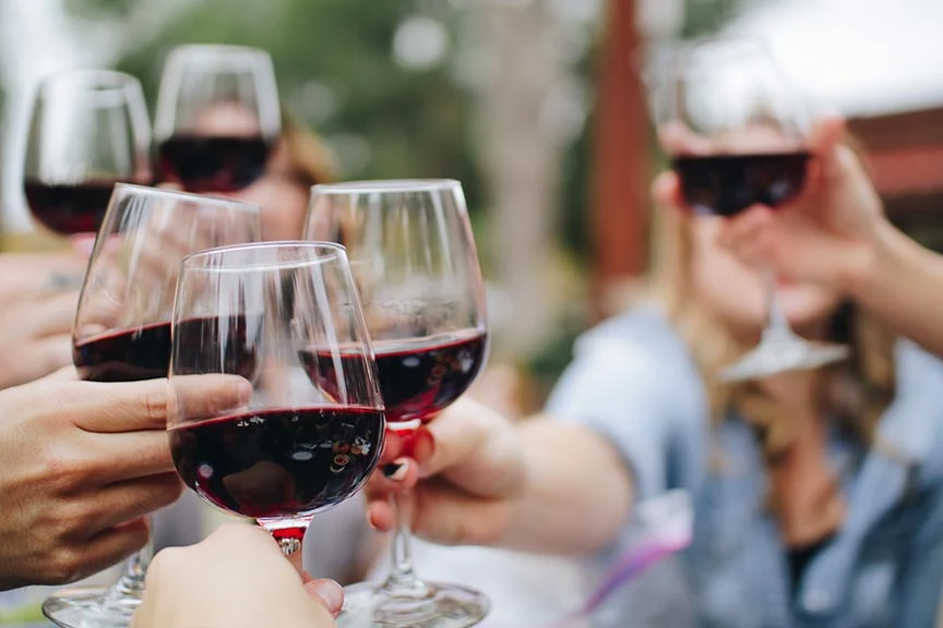 People toasting with red wine in clear wine glasses