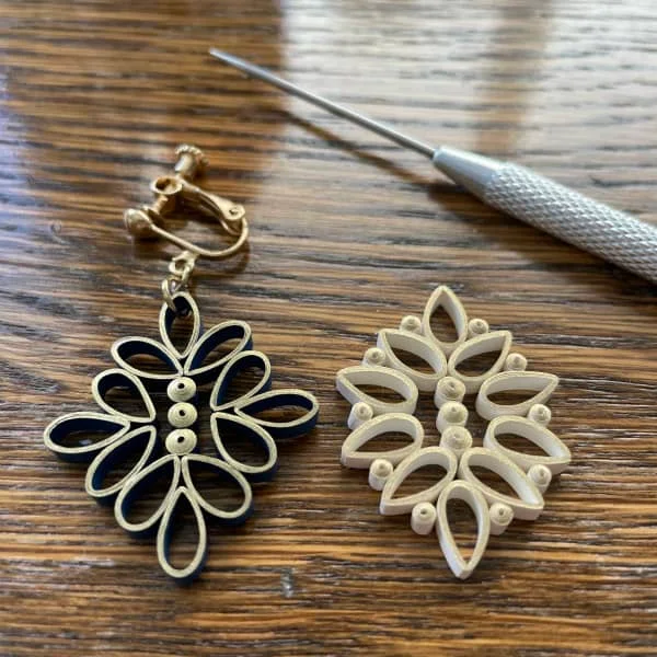 two different quilled earrings on wooden surface with clay modeling tool