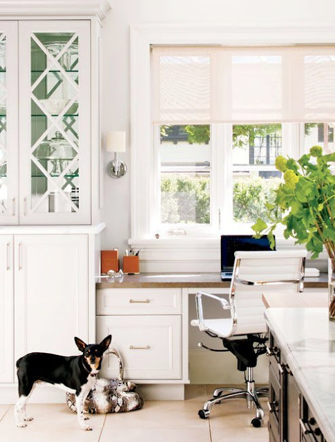 Home office in the kitchen with cabinets, a rolling chair and a white desk facing a window