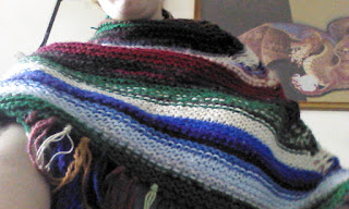 A shawl wrapped around the shoulders and neck of a person. The shawl is a number of various colours and stripes of various thickness, and the bottom edge of the shawl is fringed.