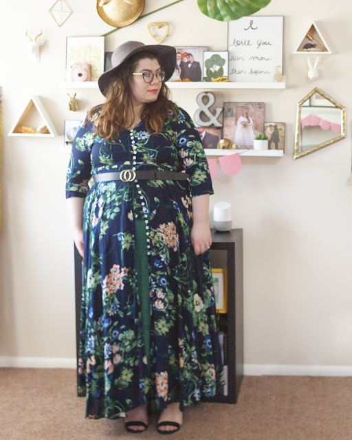An outfit consisting of a grey wide brim hat, a 3/4 sleeve green and cream floral print on navy blue maxi dress buttoned half way over a green tiered maxi dress and black sandal heels.
