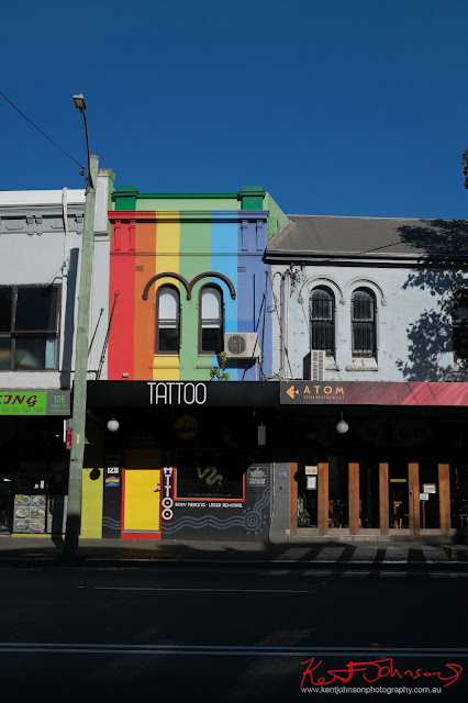 Tattoo shopfront painted in horizontal stripes of rainbow colours. Fujifilm X100VI in Newtown
