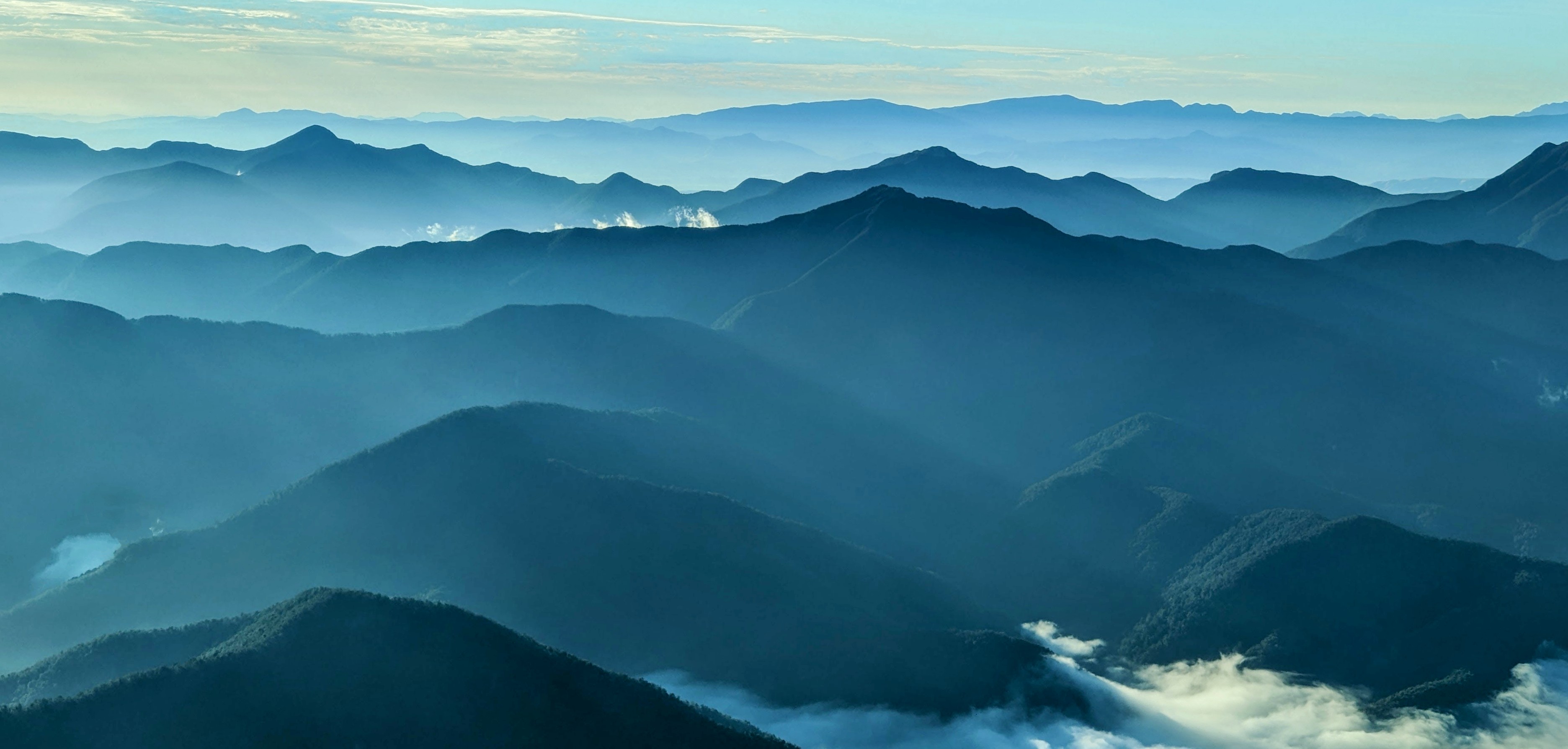 Blue hills fading in the distance of a sunrise with low cloud nestling in the close valleys, all seen from a plane
