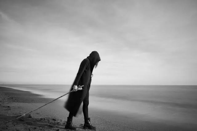 An image of a girl in the black hoodie and holding a stick walking near the beach- sad girl dp