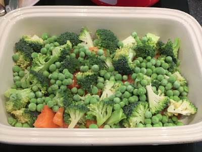 broccoli and peas layered over salmon in a casserole dish