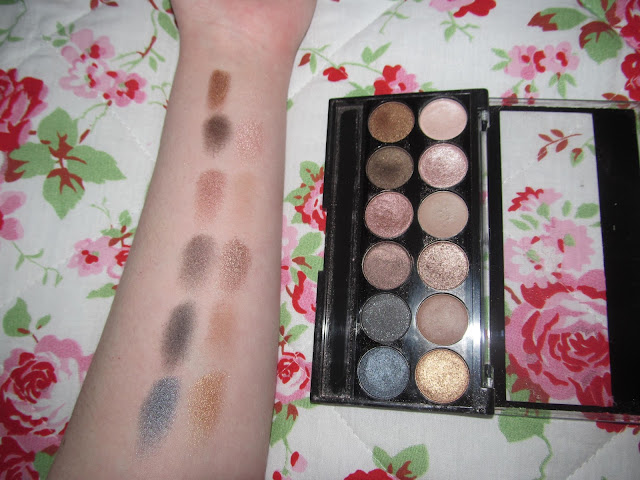 12 eyeshadow shades - cream, pale pink shimmer, dark pink shimmer, khaki, matte cream, shimmer denim blue, shimmer navy, deep purple/brown shimmer, matte light brown and shimmer gold - swatched on white forearm. photograph taken with flash to highlight shimmer