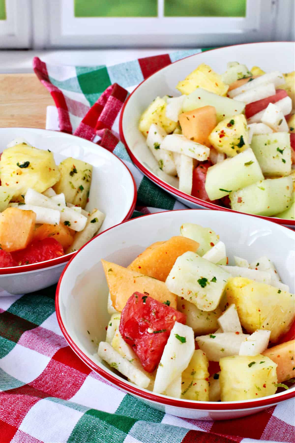 Melon, Jicama, and Pineapple Salad in a red rimmed bowl on a red and green cloth.