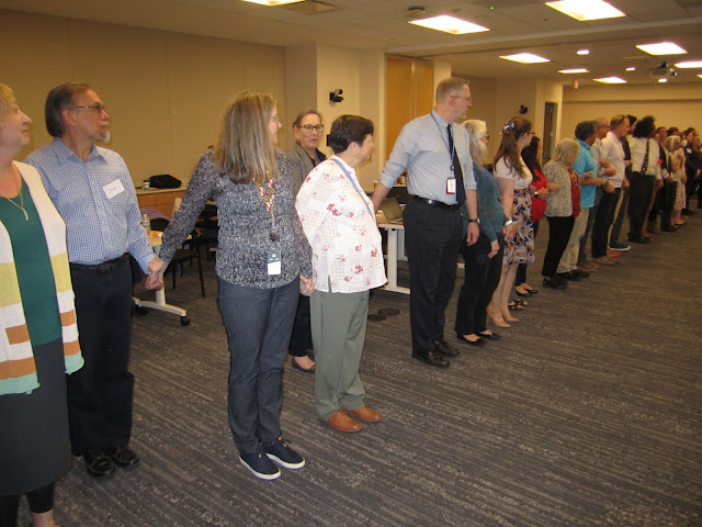 A group of people stand hand-in-hand in a line as part of a workshop.