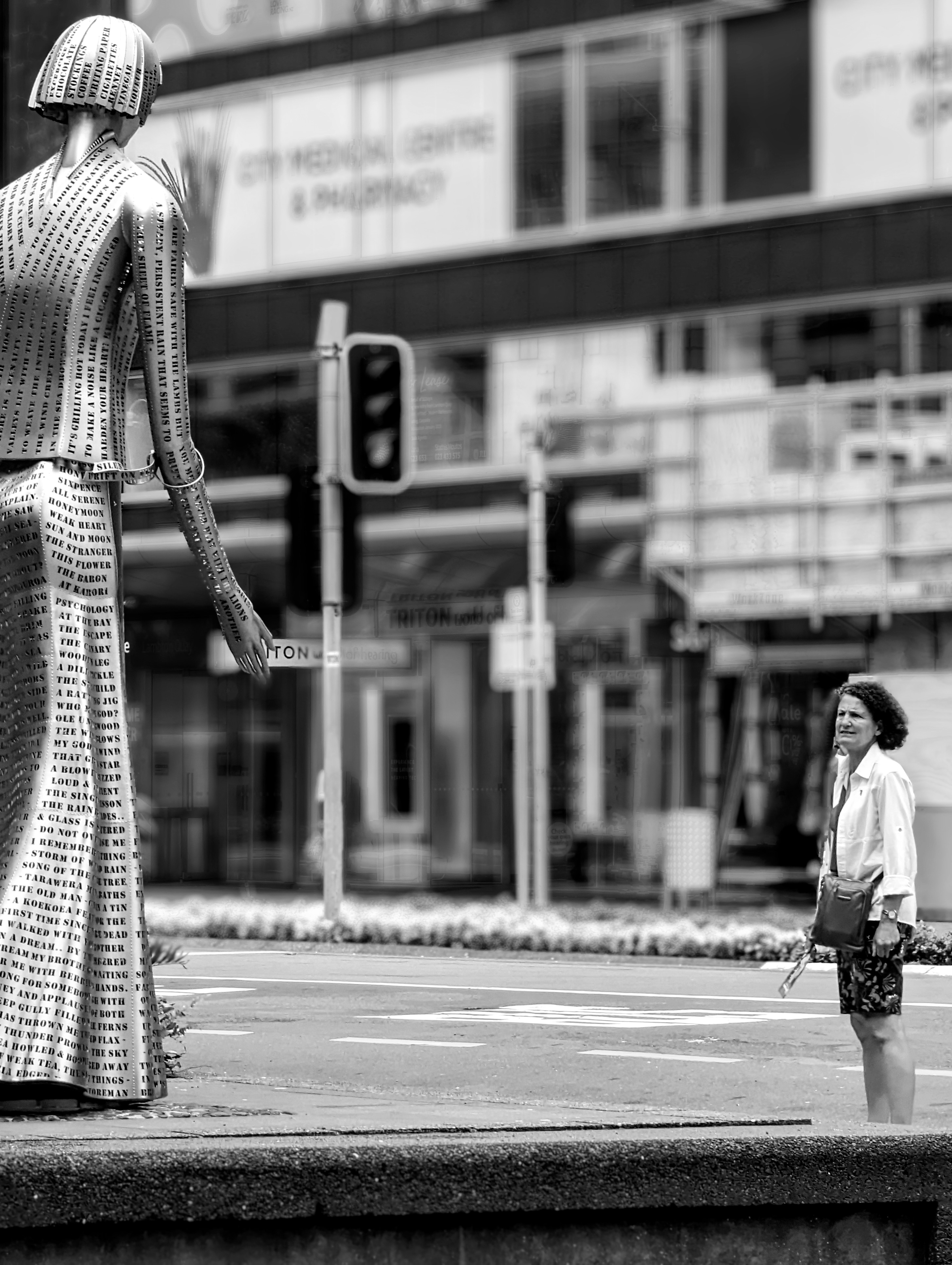 Edited version of a photo of a woman on a busy Wellington shopping street looks at the Katherine Mansfield statue. The photo is now black and white, people have been removed except the woman, and the background is blurred.