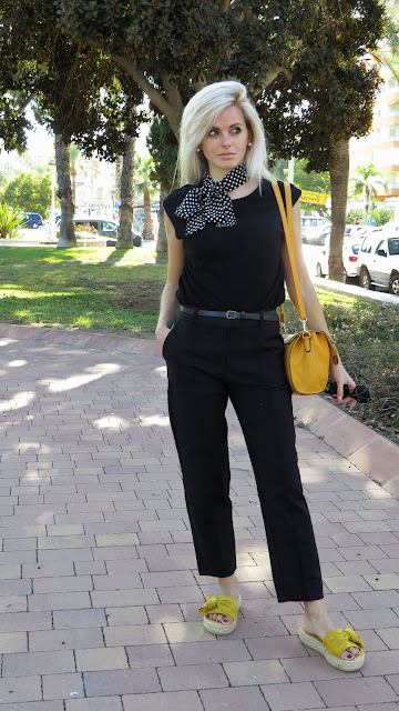 Alejandra Colomera con camiseta negra, pantalón formal negro, lazo en el cuello negro con lunares blancos y complementos mostaza