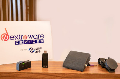 Mouseware, is a head-mounted wearable devices that allows handsfree use of mouse. Seen in image the device with accessorie placed on a table with background of Brand Logos etc.