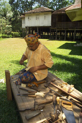 Malay man dressed in traditional garment making a traditional keris in a traditional Malay kampong