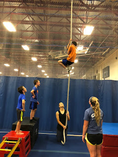 One athlete climbing rope with two spotters below and two athletes looking on