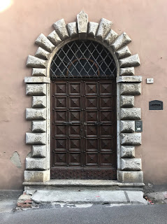 foto de uma porta de madeira com detalhes de pequenos quadrado e arco com decoração de pedras de tamanhos alternados