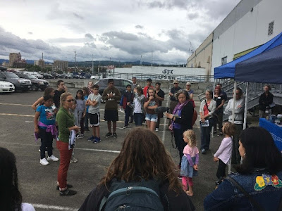 Adults and children gathered outside listening to someone talk.