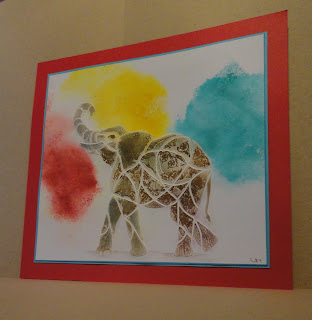 Gilded elephant image over bursts of red, yellow, blue, mounted on blue and red