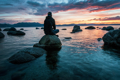 Hombre sentado en una roca mirando al mar al atardecer