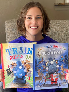 author Jodi Adams holds up her two picture books, the Little Train Engine Rolls On and The Little Train Engine Rolls On to the North Pole