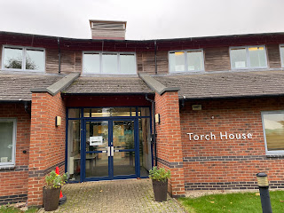 A building with a glass fronted door, and a sign reading 'Torch House' on the wall