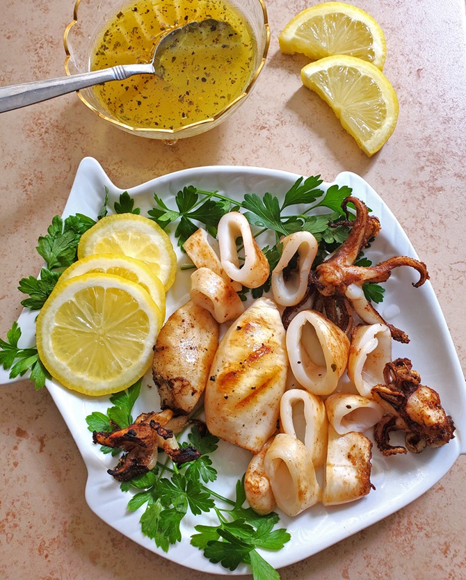 calamari marinated then grilled on a fish white dish with lemon wedges and parsley