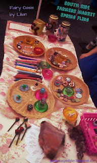 Side image of a table covered with white and pink floral fabric.  Lots of polymer clay things are set up on it for sale.  