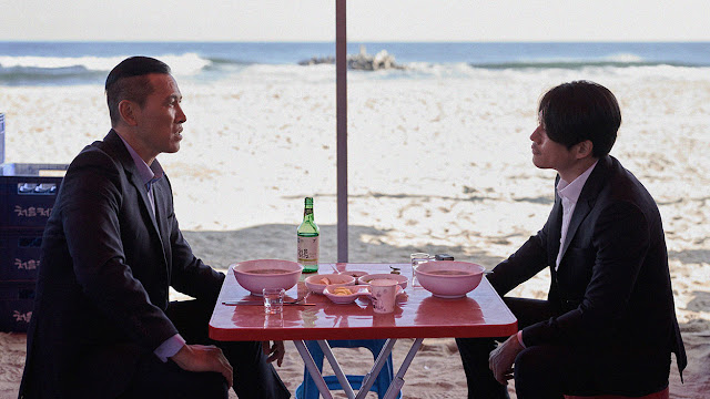 two men eating at a table on a beach