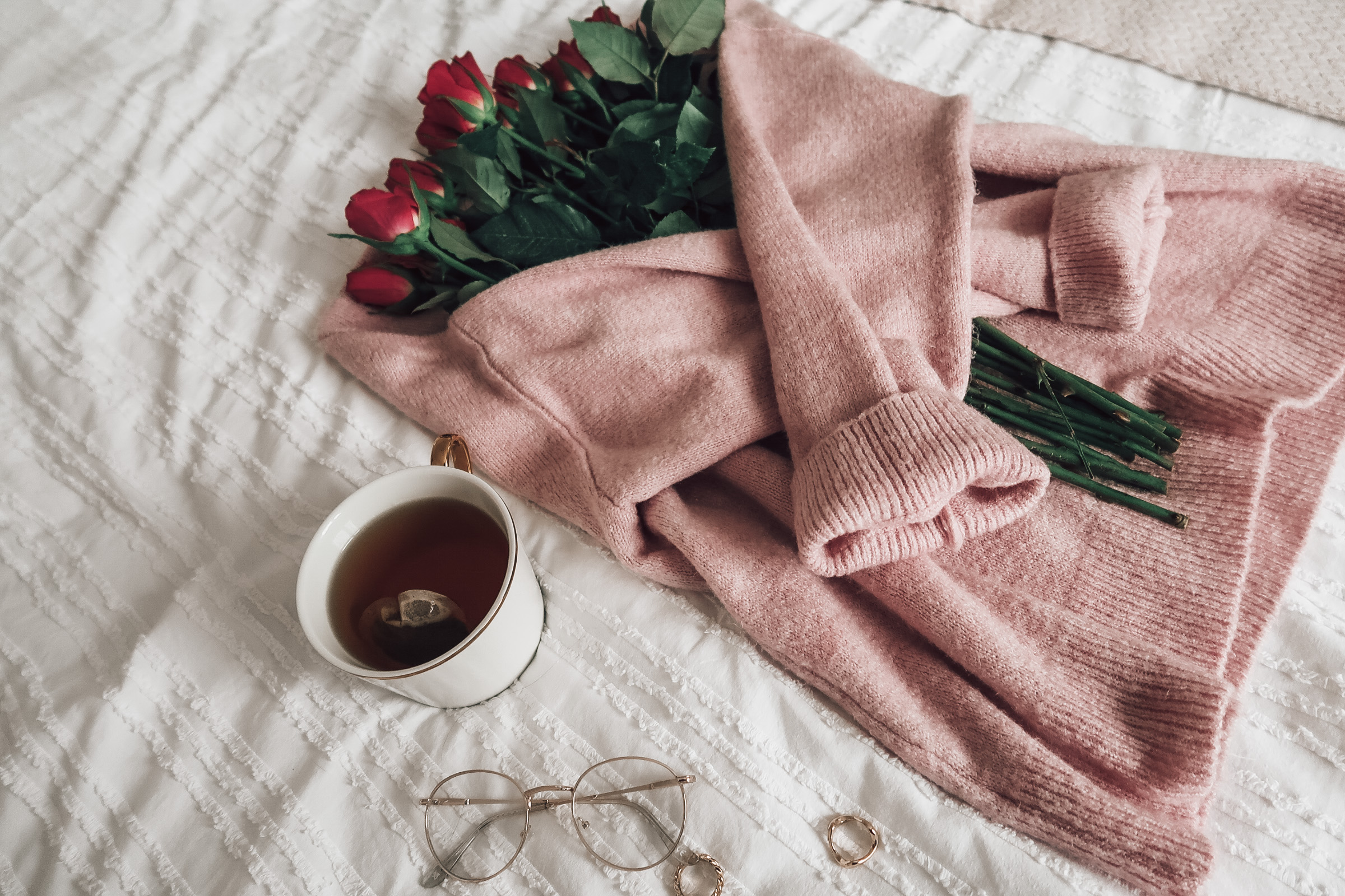 A rose pink jumper wrapped around a bouquet of pink tulips next to a white mug.