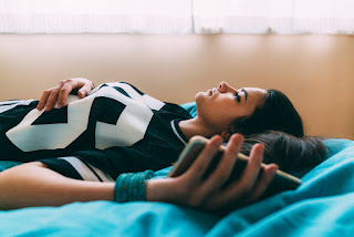 Lady lying on bed, staring upwards and thinking with her phone in her hand.