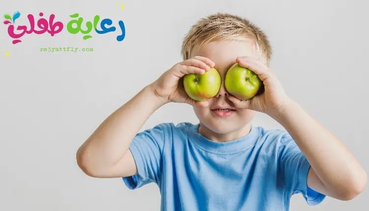 صورة ولد صغير ممسك بتفاحتين ويضعهم أمام عينيه، كتعبير منا عن فوائد الفواكه للأطفال.