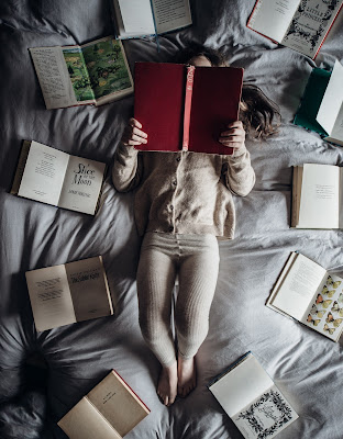 Mujer rodeada de libros abiertos leyendo en la cama