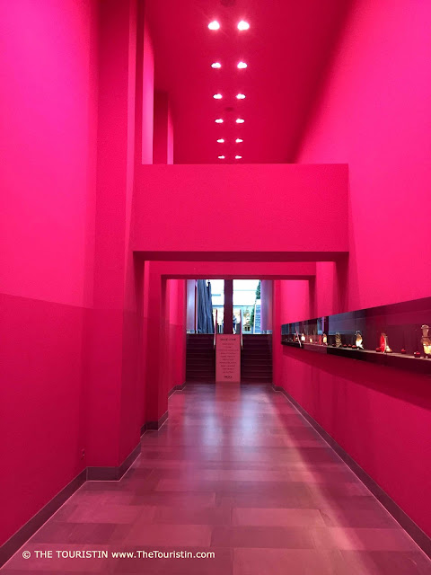 A modern long and high dark pink coloured hallway decorated with ceiling spotlights.