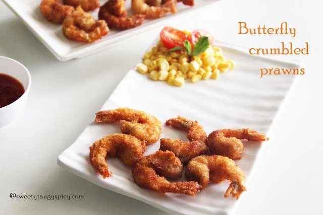 A tempting plate of golden-brown butterfly crumbed prawns served with a side of colorful corn salad and a bowl of tomato ketchup for dipping, a delightful seafood dish with fresh accompaniments.