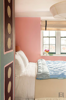 Beata Heuman bedroom with salmon pink walls, hand painted door, fabric light, and blue down comforter layered on bed