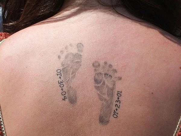 una mama de espaldas, vemos en su espalda un tatuaje de las huellas de sus bebes