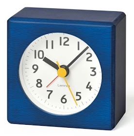 square blue alarm clock, round white dial, yellow second hand, red alarm indicator