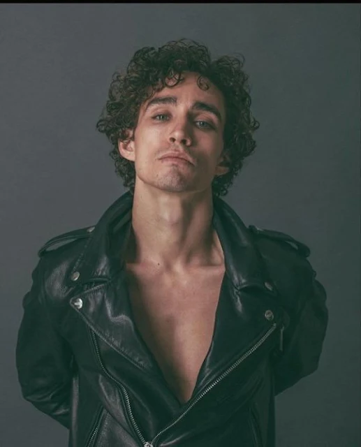 From the chest up of a brown hair curly haired model wearing black leather biker jacket shirtless
