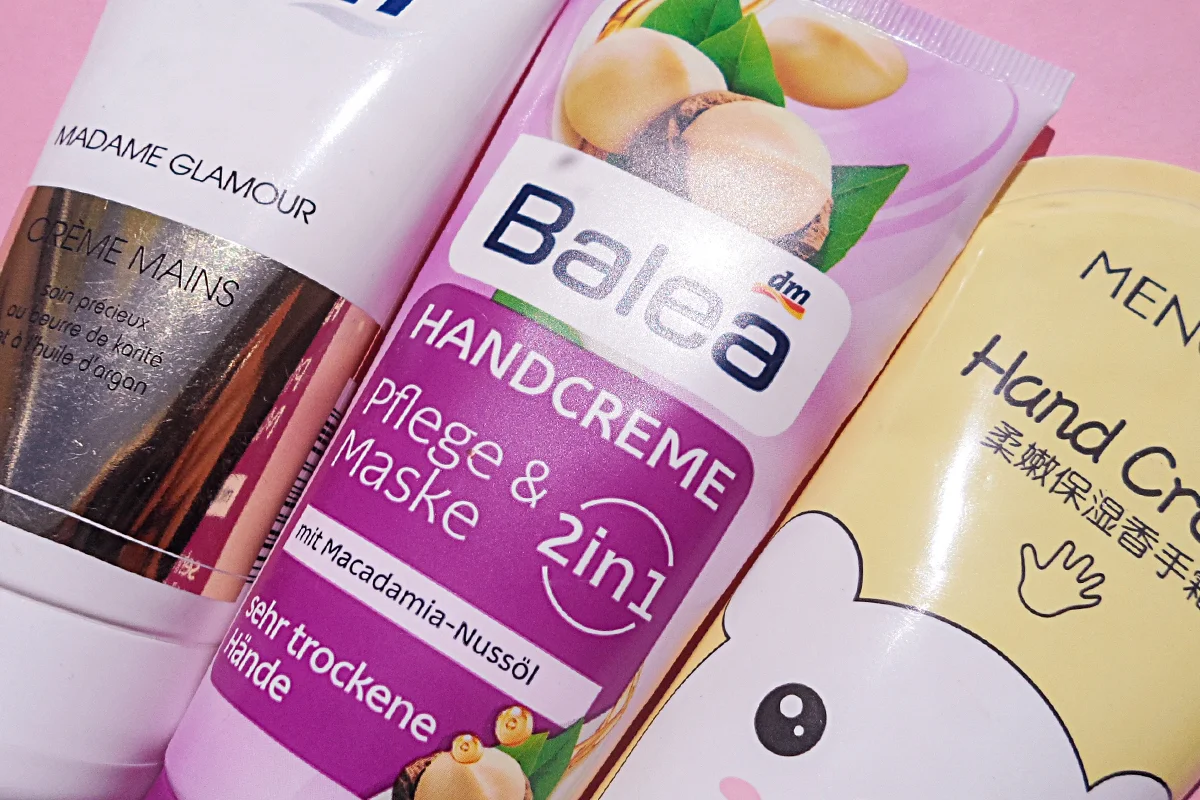 close-up shot of three hand creams laying on top of a pink table