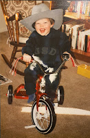 A young boy wearing a Stetson hat while riding a tricycle