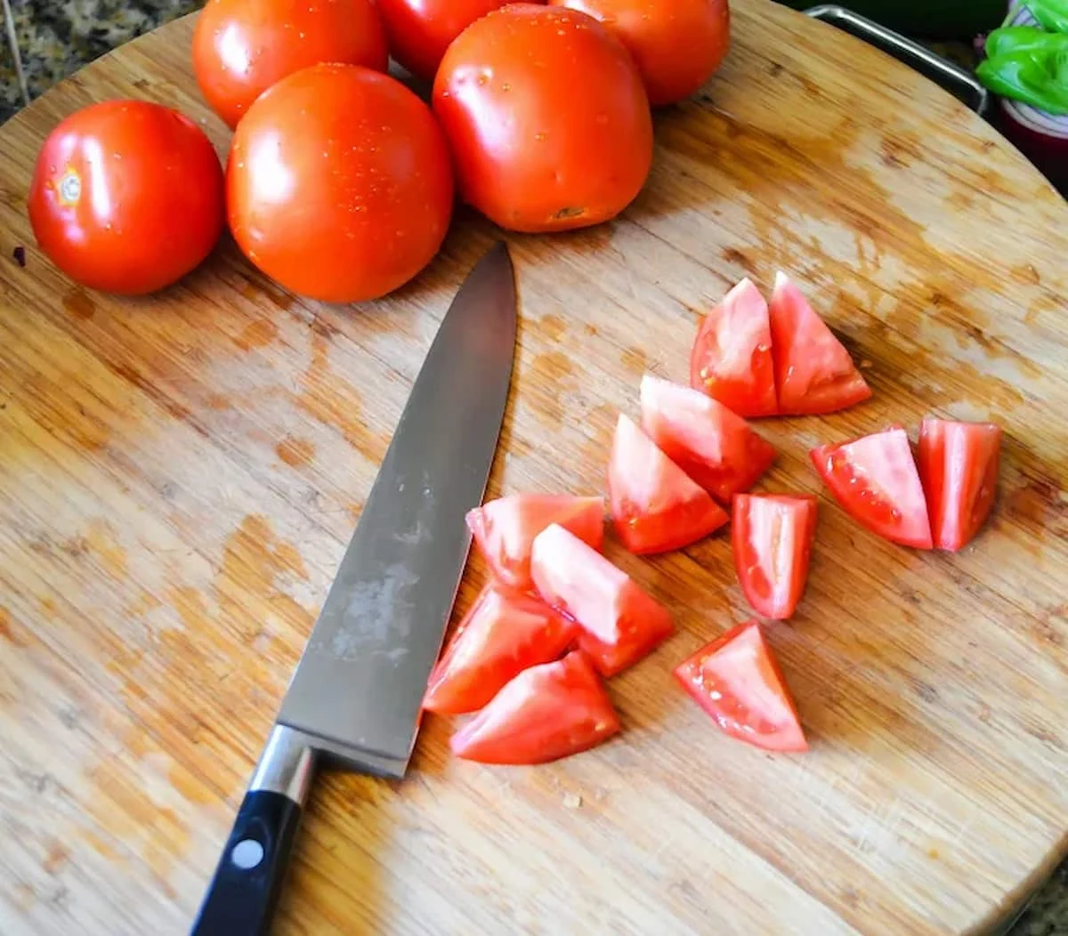 Tomatoes sliced into cubes on a wooden cutting board with a knife resting on board.