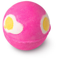 A pink spherical bath bomb with white and yellow circular egg salt shapes on a bright background