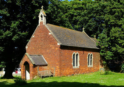 small red brick church with concrete tiled roof and bellcote, two pairs of lancet windows at the side