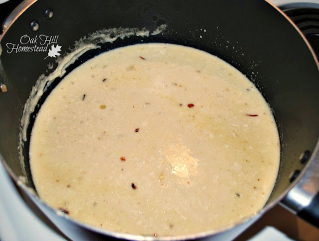 Broccoli and cheddar cheese soup: the chicken broth is whisked into the roux, in a black saucepan.