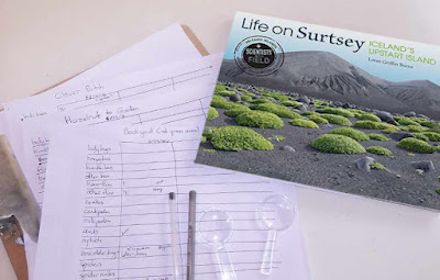 A picture of a children's book title Life on Surtsey, laying on top of a clipboard with papers.