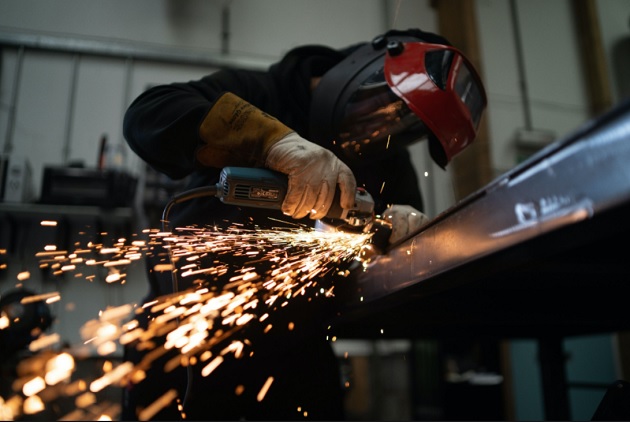 A worker is grinding metal in a workshop which can be an indicator for metal demand and supply.