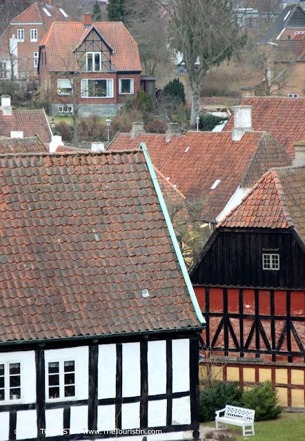 A white park bench next to a group of medieval red-roofed timbered white-, red-, and orange houses.