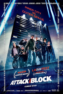 A group of people stood in front of a block of flats, lit up by various lights. The text reads 'Inner City Vs. Outer Space' 'Attack The Block'.