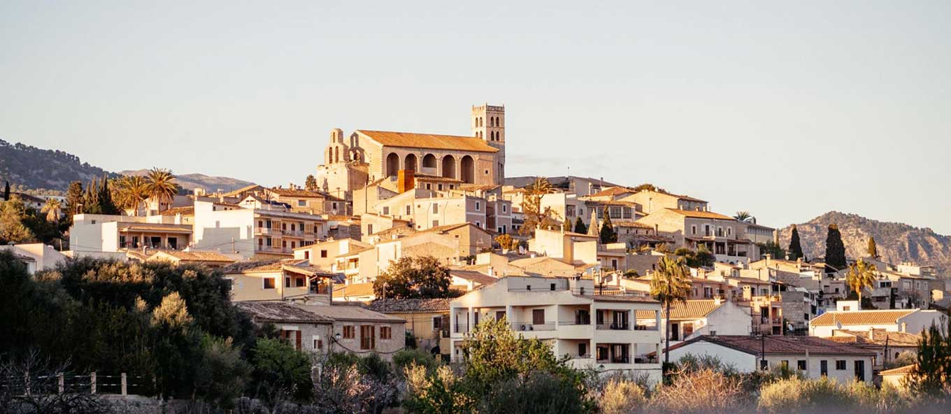 A photo taken of a sunny hillside in Spain that has various different properties situated on it and a religious building in the middle.