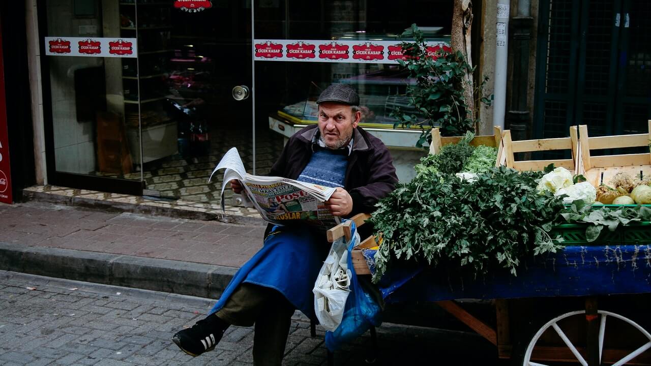 Street vendor with newspaper near fresh herbs in food cart | 20 Street Photography Tips