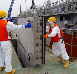 In this June 12, 2011 photo released on July 5, 2011 by Tokyo Electric Power Co., masked workers in protective outfits prepare to drop one of sliding concrete slabs into a slit of the upper part of the sluice screen for Unit 2 reactor at the tsunami-crippled Fukushima Dai-ichi nuclear power plant in Okuma, Fukushima Prefecture, northeastern Japan, in their effort to decrease the leak of radiation contaminated water to the ocean. (AP Photo/Tokyo Electric Power Co.)